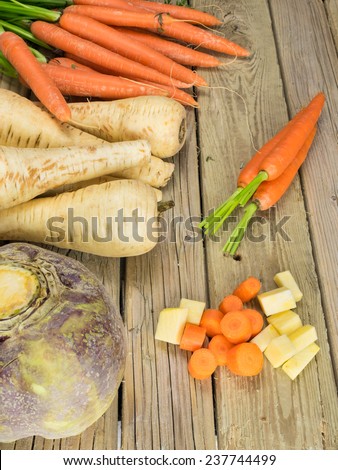 winter root crops  against aged wooden background with peeled and sliced vegetables