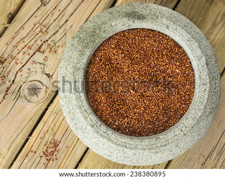 close up overhead view of red quinoa in a rustic stoneware bowl against a cracked aged wooden table top with spilled quinoa seeds