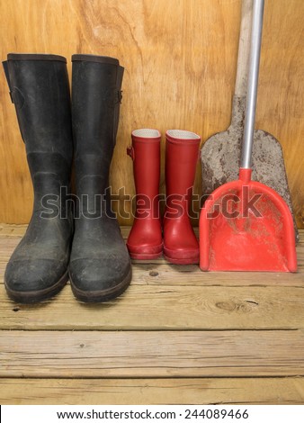 mans green rubber boots and childs red rubber boots in a shed with tools father and son concept