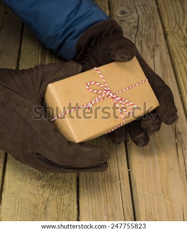 detail of mans hands in winter coat and gloves holding a string and brown paper parcel over a rustic wooden table