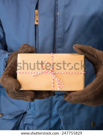 detail of mans hands in leather gloves holding a string and brown paper parcel with blue winter coat behind