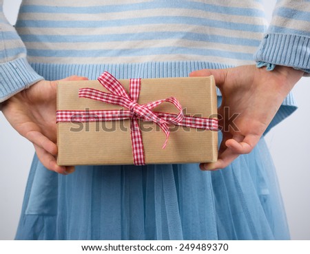 detail of small girl holding a present wrapped in brown paper with a check ribbon behind back