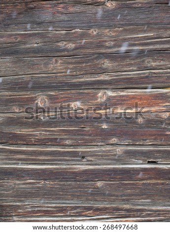 knotted aged dark wooden cabin wall with falling snow with movement blur in foreground