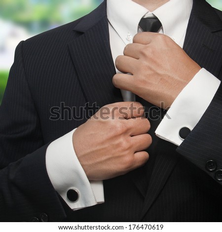 a man in a black suit straightens his tie