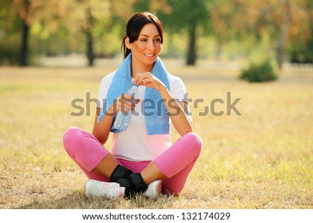 Young woman resting after exercising and holding water bottle
