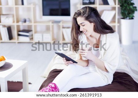 Beautiful woman in bed having tablet computer and laughing, Woman in bed text messages with  tablet and laughing in living room