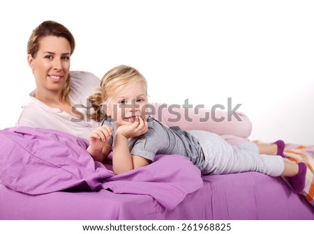 Cute little girl with her mother lying on a bed, Attentive mother hugging her daughter lying on a bed