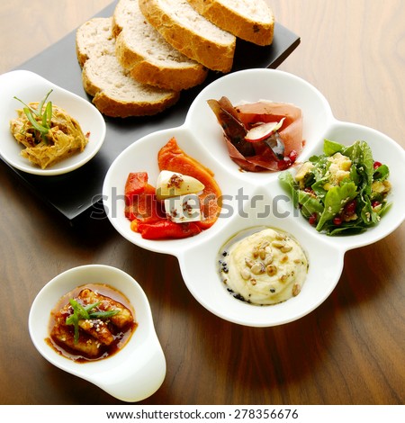 Mixed food on a white and a black plate with ham, yellow dressing, chicken in spicy sauce with sesame seeds and paprika on which pieces of cheese, mint and parsley