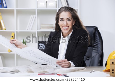 Female Architect Studying Plans In Office. Woman architect working in her office,looking at camera and smiling