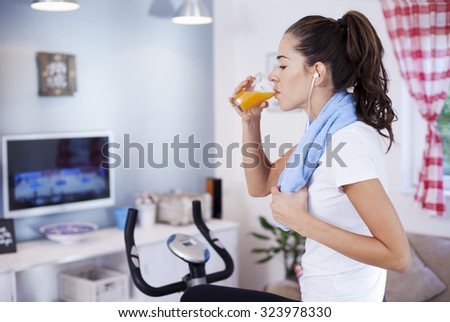 Lovely woman drinking orange juice while training on an exercise bike in her living room at home