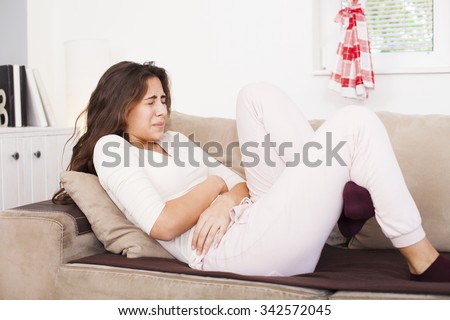 Young woman sitting on the bed with hard stomach pain