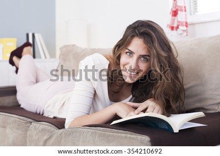 Charming beautiful woman reading a book lying on a sofa in the l