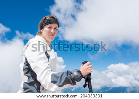 Young woman holding a trekking pole in her hand and watching into the camera