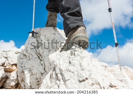 Close up of hiking shoes and trekking poles ascending a mountain