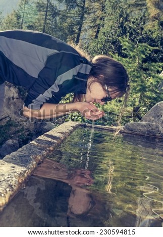 Young girl drinking alpine clean water from a concrete sink