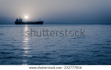 Cargo ship sailing with full moon rising above it