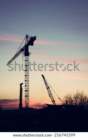 Industrial construction site at sunset with silhouette of a crane.