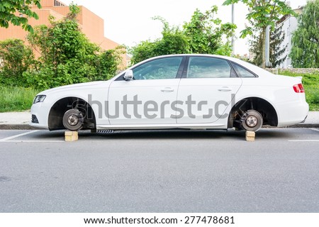 Car with stolen wheels. White vehicle left on wooden bricks.