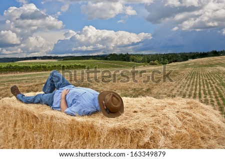Man with cowboy hat taking a nap on a stack of hay on country farm/Man with cowboy hat sleeping on hay in country