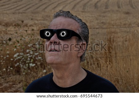 Man viewing full solar eclipse with solar glasses in country field/Man looking at full solar eclipse with eclipse reflecting in lenses