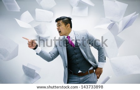 angry businessman with pile of papers flying on air