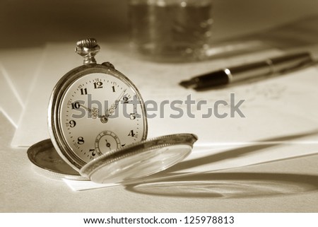 Old watch on a table, in the background a letter, a pen and a glass. Picture is in a warm duo-tone setting.