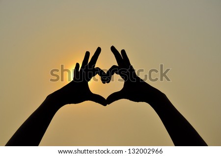Hands in heart shape with silhouette and shadow with sun in background