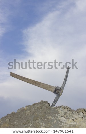 Symbol for: success, finally done and good job. Pickaxe with broken handle of hard work in the heap of ground against blue sky