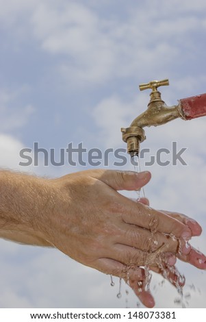 Human hands under water tap with a beautiful sky background