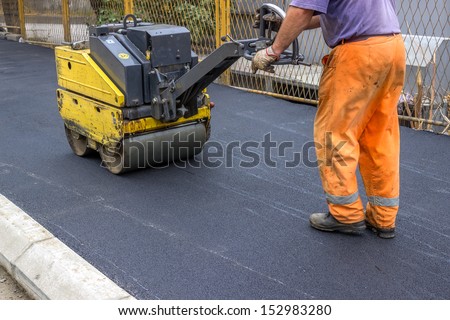 Road construction worker behind construction roller, leveling new asphalt on sidewalk