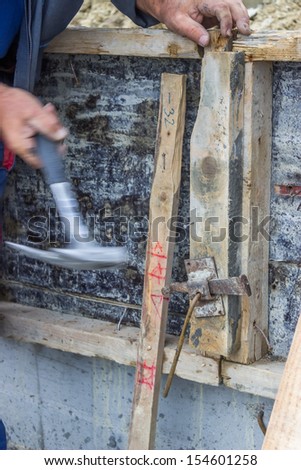 Builder hammering a nail into a piece of wood at Construction Site