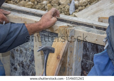 Builder hammering a nail into a piece of wood at Construction Site
