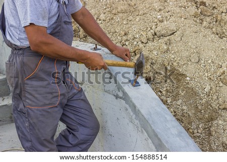 A construction worker uses a hammer to knock metal holders in a concrete for hand railings of new stairs