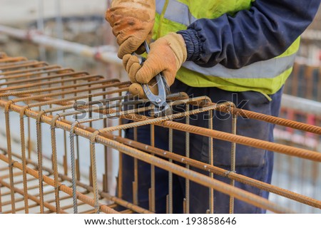 workers hands using steel wire and pincers to secure rebar before concrete is poured over it