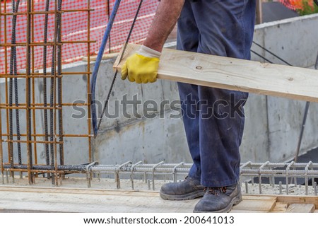 Bulder worker sawing wood board with hand saw, working on formwork installation. Selective focus and motion blur.