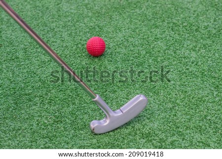 Red golf ball on golf course with mini golf stick