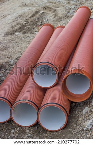 Stack of orange underground plastic pipes at construction site