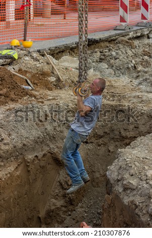 BELGRADE, SERBIA - AUGUST 03:  Excavator arm lifting construction worker from trench on chains with hooks.  Pipeline construction at street Vojvode Stepe, Belgrade, Serbia  in August 2014.