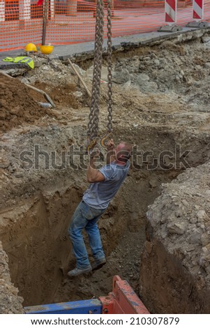 BELGRADE, SERBIA - AUGUST 03:  Excavator arm lifting construction worker from trench on chains with hooks.  Pipeline construction at street Vojvode Stepe, Belgrade, Serbia  in August 2014.