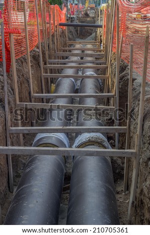 Pipes in trench, industrial pipeline. Insulated pipes to connect a new buildings on heat system. One insulated pipe carries hot water, another carries cool water.