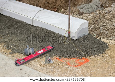 Tools for installing concrete curb stone and string with metal stakes to level at sidewalk construction site. Selective focus.