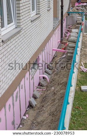 Trenching around building for new layer of foam insulation, fitting styrofoam thermal insulation