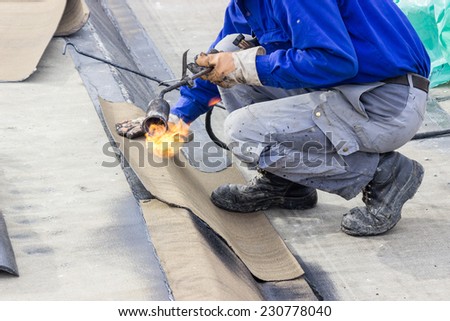 Insulation worker with propane blowtorch at floor slab waterproofing works. Worker heating and melting bitumen felt. Water proofing of concrete structure.