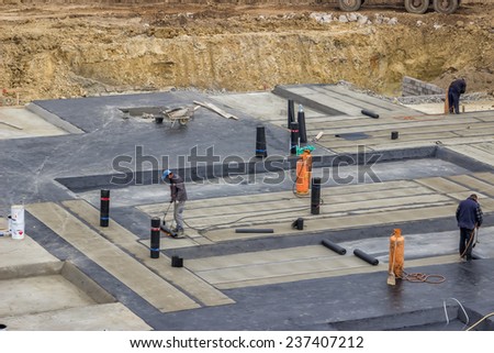 BELGRADE, SERBIA - OCTOBER 30: Foundation insulation workers at ground waterproofing works. Workers melting bitumen felt and water proofing of concrete structure. At construction site in October 2014.