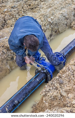 Worker installing water pipe valve in a trench. Laying a water pipeline. Selective focus. At construction site.