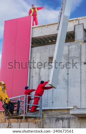 BELGRADE, SERBIA - DECEMBER 27: Builders on aerial access platform connecting red wall sandwich panels. At construction site in December 2014.