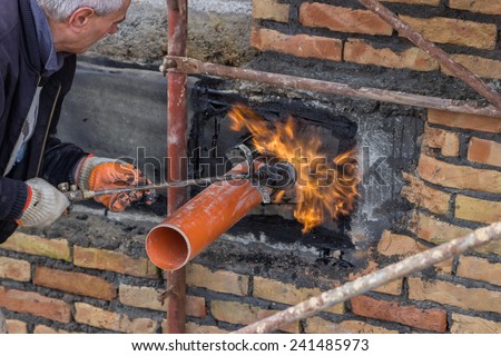 BELGRADE, SERBIA - DECEMBER 26: Insulation worker with propane blow torch melting bitumen felt around pipe on the basement wall. At construction site in December 2014.