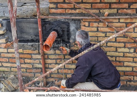 BELGRADE, SERBIA - DECEMBER 26: Insulation worker heating and melting bitumen felt around pipe on the basement wall. At construction site in December 2014.