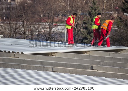 BELGRADE, SERBIA - DECEMBER 13: Roof sheet metal workers,  using electrical drills to screwing down panels. Fastening metal roofing. Selective focus. At construction site in December 2014.