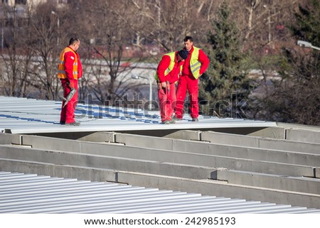 BELGRADE, SERBIA - DECEMBER 13: Roof sheet metal workers,  using electrical drills to screwing down panels. Fastening metal roofing. Selective focus. At construction site in December 2014.